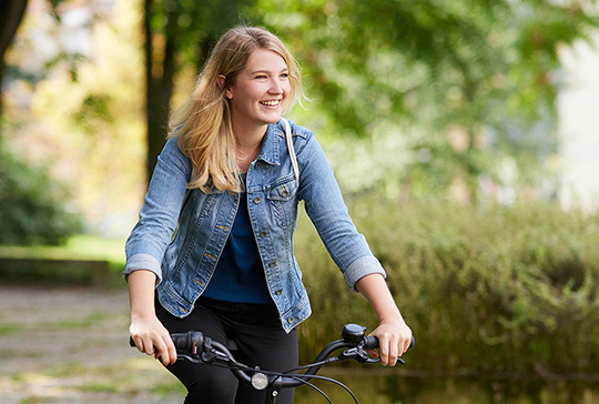 eine Dame fährt auf Ihrem Fahrrad und blickt erfreut auf ihre Zukunft